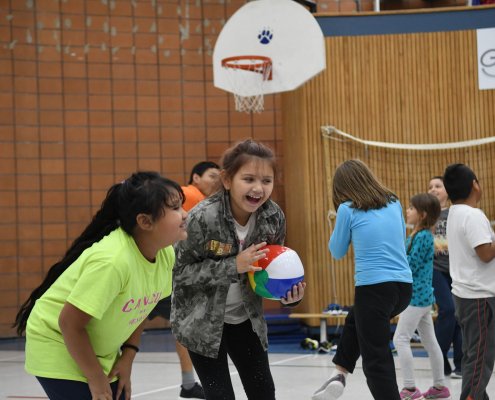 "A group of kids playing with beach balls in the gym, laughing and having fun as they toss the balls to each other."